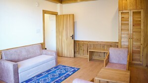 Een kamer met een houten plafond, een beige bank, een houten bankje en een houten tafel.