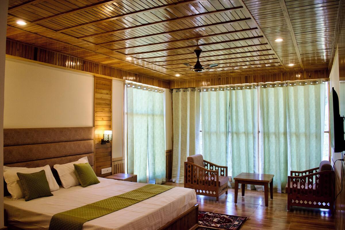 A hotel room with a wooden ceiling, a large bed with pillows, a chair, a small table, and a television.