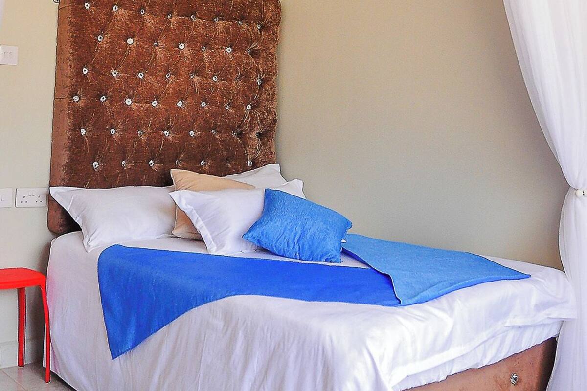 Une chambre à coucher avec une tête de lit capitonnée, un lit recouvert d’une literie blanche et bleue, et un ciel de lit blanc.