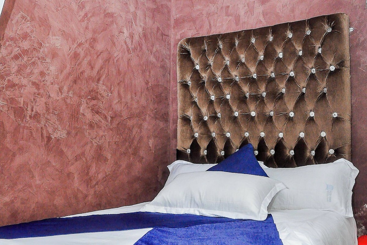 Une chambre à coucher avec une tête de lit capitonnée, du linge de lit blanc et un plaid bleu.