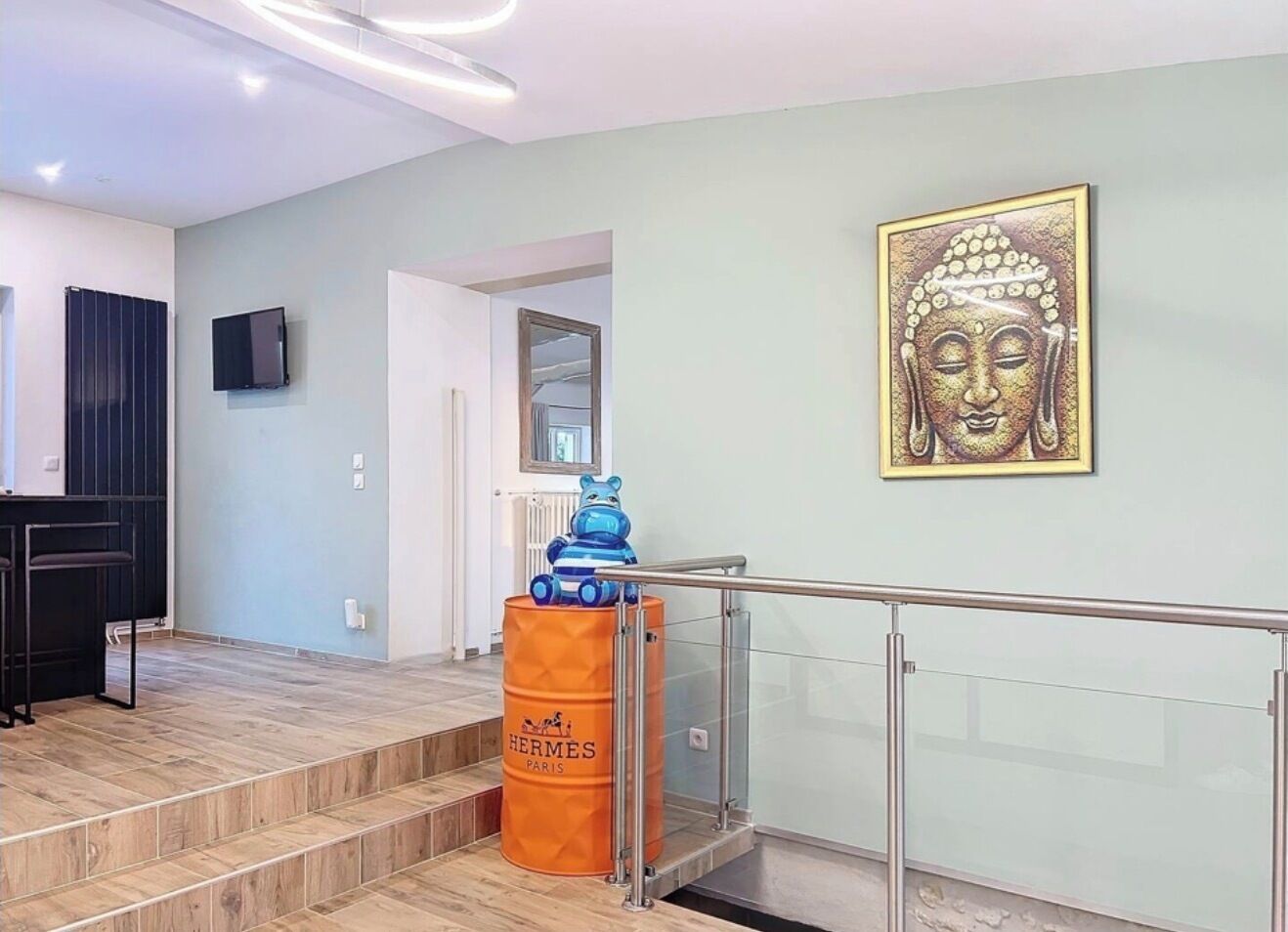A modern interior with a staircase, a framed Buddha artwork, and a Hermes barrel.