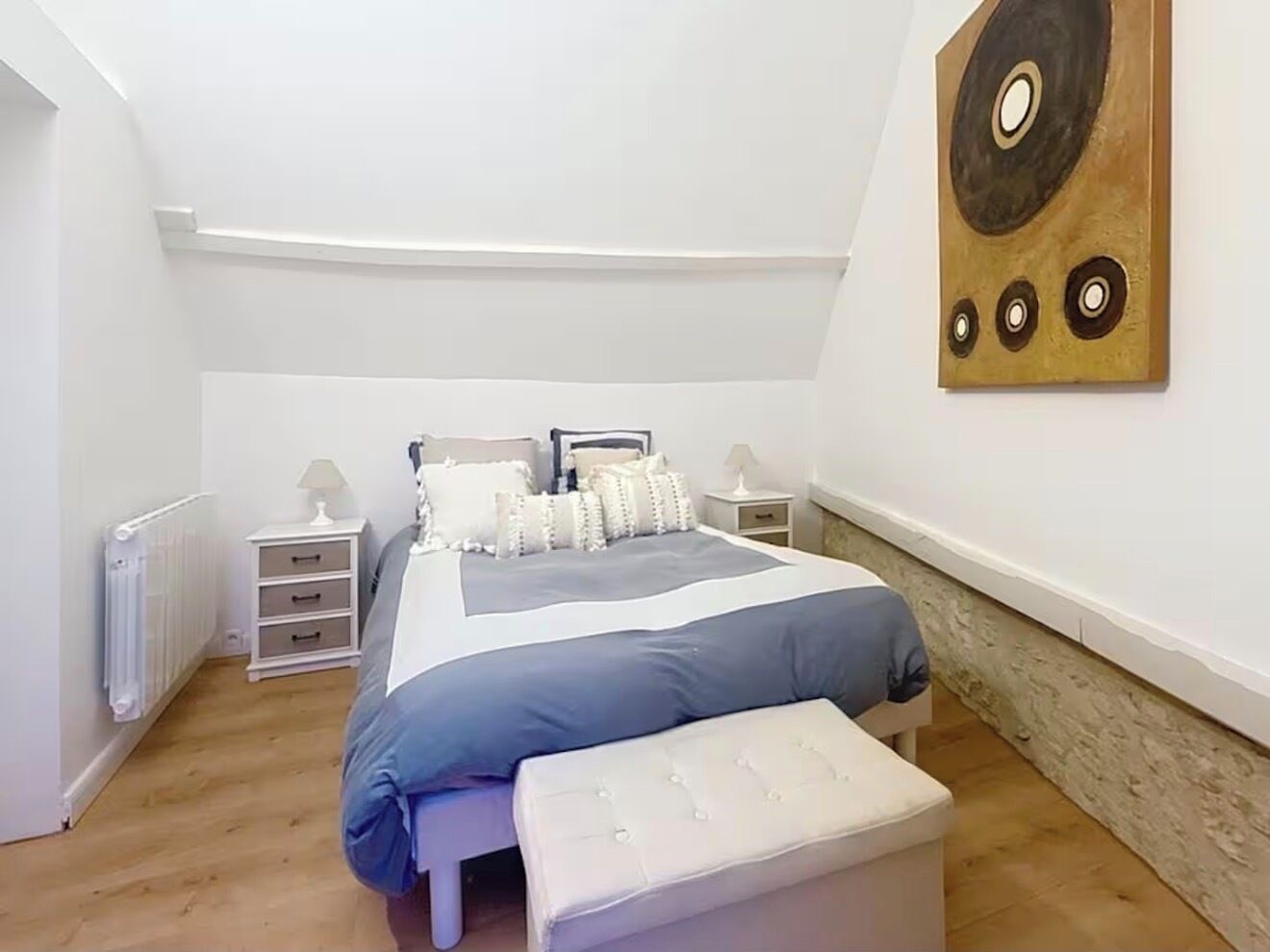 Une chambre à coucher comprenant un lit, des tables de chevet, un radiateur et une œuvre d’art murale.