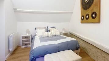 Une chambre à coucher comprenant un lit, des tables de chevet, un radiateur et une œuvre d’art murale.
