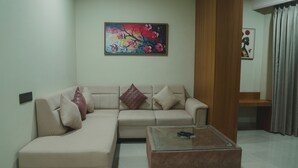 Un salon avec un canapé beige, une table basse en verre et deux tableaux accrochés au mur.