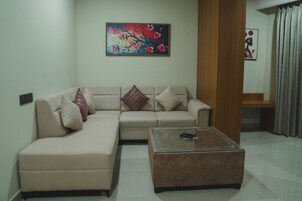 Uma sala de estar com um sofá bege, uma mesa de centro de vidro e duas pinturas na parede.