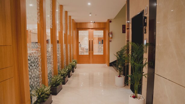 Un couloir aux murs lambrés, agrémenté de plantes en pot, et une porte donnant sur une pièce.
