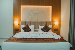 Quarto de hotel com uma cama grande, duas luminárias fixadas na parede e uma cabeceira decorativa.