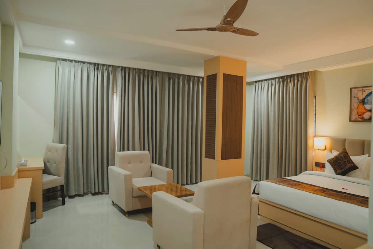 A hotel room with a bed, two armchairs, a small table, a ceiling fan, and a large window with curtains.