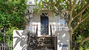 Una casa con entrada protegida por un portón, una escalera que lleva a la puerta principal y un árbol en primer plano.