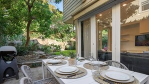 Un espacio de comedor al aire libre con una mesa blanca dispuesta para cuatro personas, rodeado de sillas de mimbre.