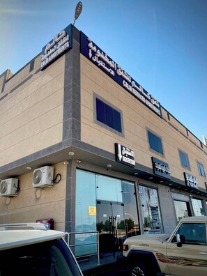 A building with a sign for 'Calm Residences' and a 'Reception' sign. There are air conditioning units on the wall, and a car is parked in front. - Calm Serviced Apartments 1 (Riyadh)