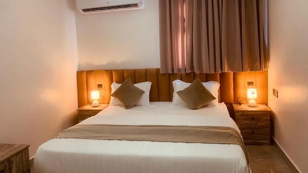 Habitación de hotel con una cama, dos mesitas de noche con lámparas, un equipo de aire acondicionado y una ventana con cortinas.