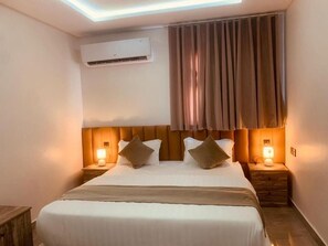 Ein Hotelzimmer mit einem Bett, zwei Nachttischen mit Lampen, einer Klimaanlage und einem Fenster mit Vorhängen.