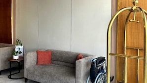 A modern interior with a grey sofa, a small table with a plant, and a wheelchair. - Calm Serviced Apartments 1 (Riyadh)