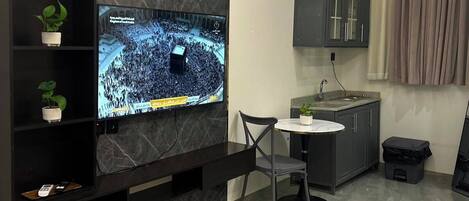 A modern kitchen with a built-in TV, a small dining area, and a grey marble backsplash.