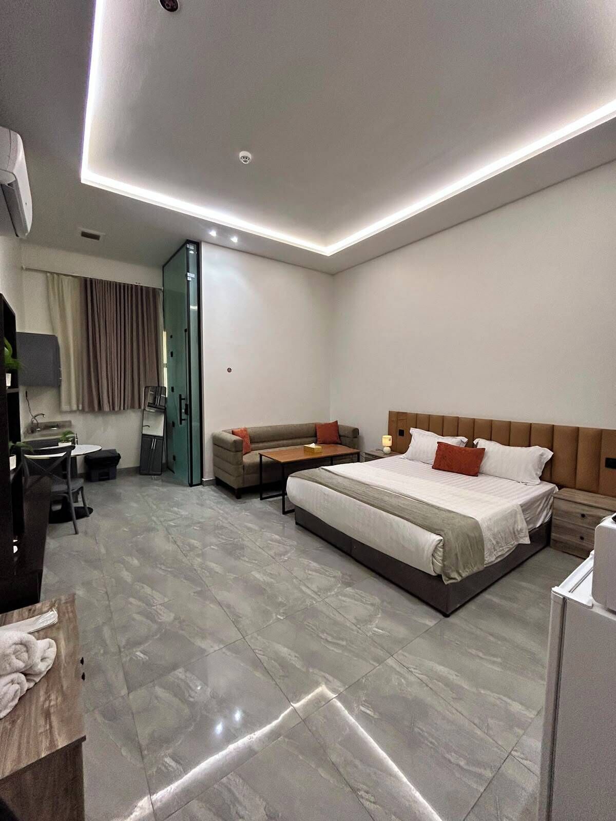 A modern hotel room with a large bed, a sofa, a desk, and a wardrobe.