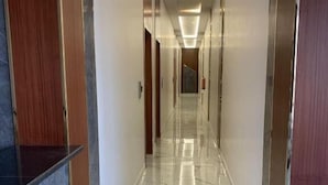 Un pasillo largo y estrecho con un suelo de mármol brillante y puertas de madera a ambos lados.