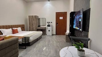 Ein Hotelzimmer mit einem Bett, einem Sofa, einem kleinen Tisch mit Pflanze, einem Fernseher und einer Mikrowelle.