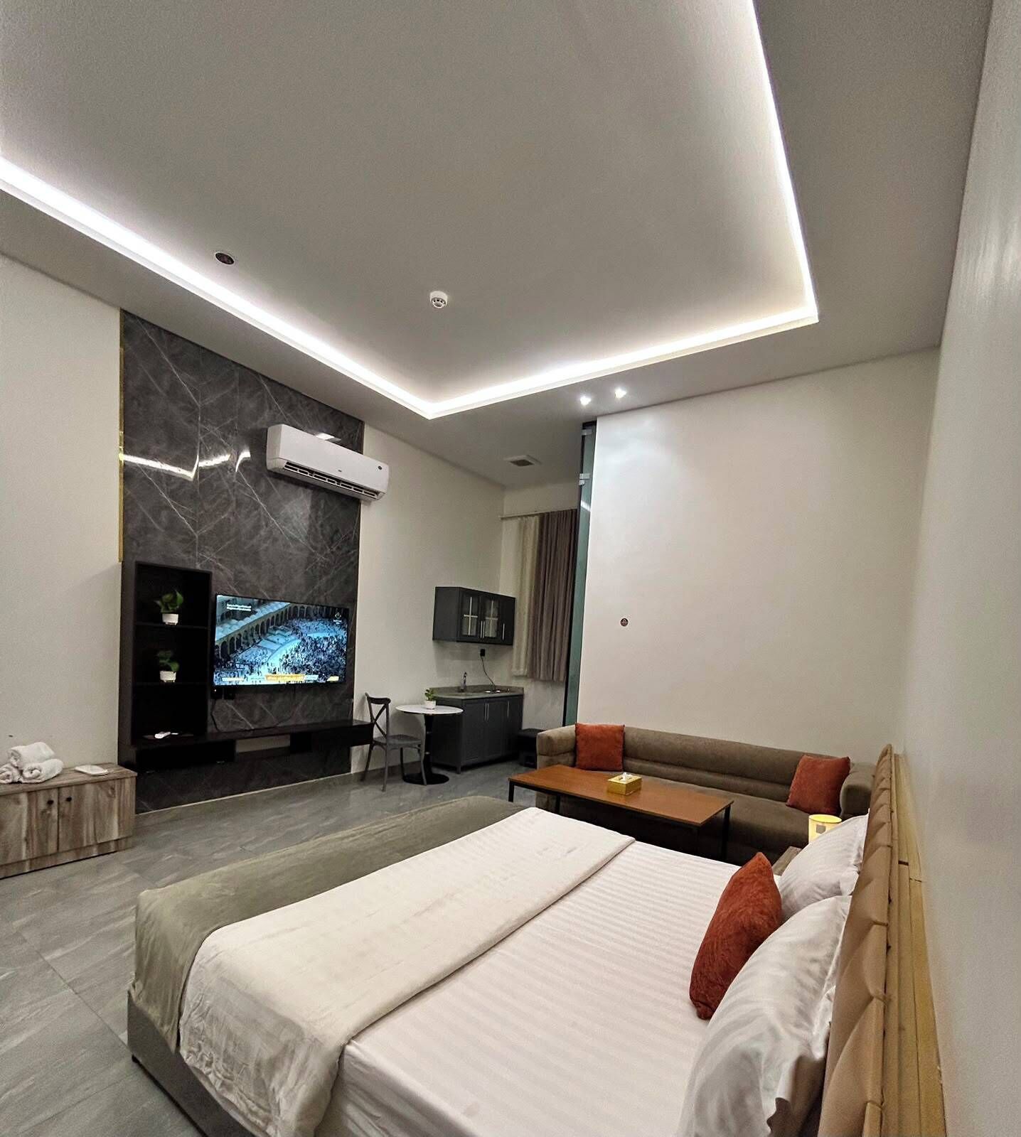 Une chambre d’hôtel moderne dotée d’un grand lit, d’une télévision à écran plat, d’une petite kitchenette et d’un coin salon avec un canapé et des fauteuils.
