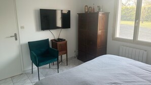 Une chambre à coucher comprenant un lit, un téléviseur fixé au mur, une armoire en bois et une fenêtre donnant sur un paysage verdoyant.