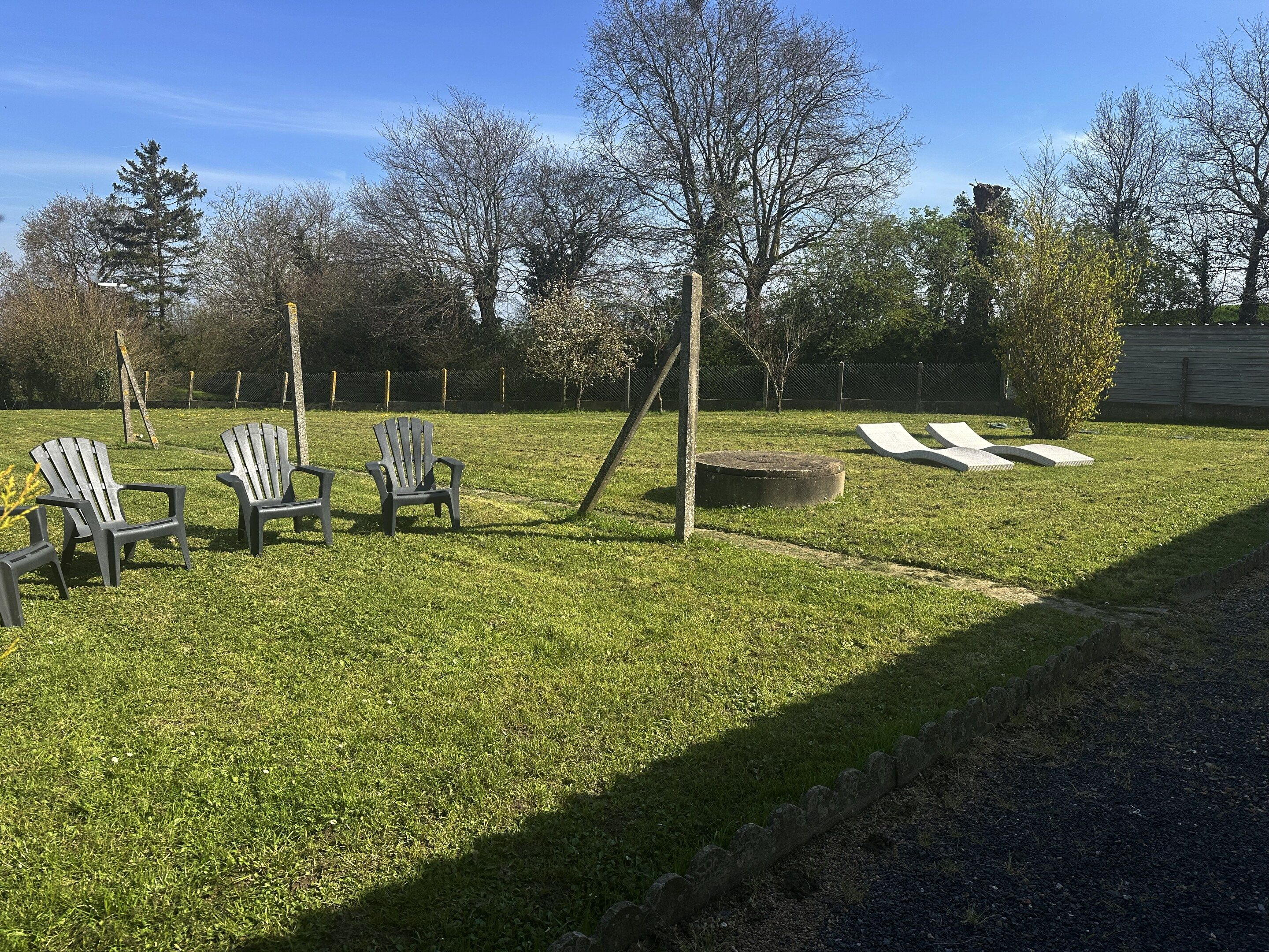 A grassy outdoor area with Adirondack chairs, a concrete planter, and a wooden post.