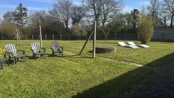 A grassy outdoor area with Adirondack chairs, a concrete planter, and a wooden post.