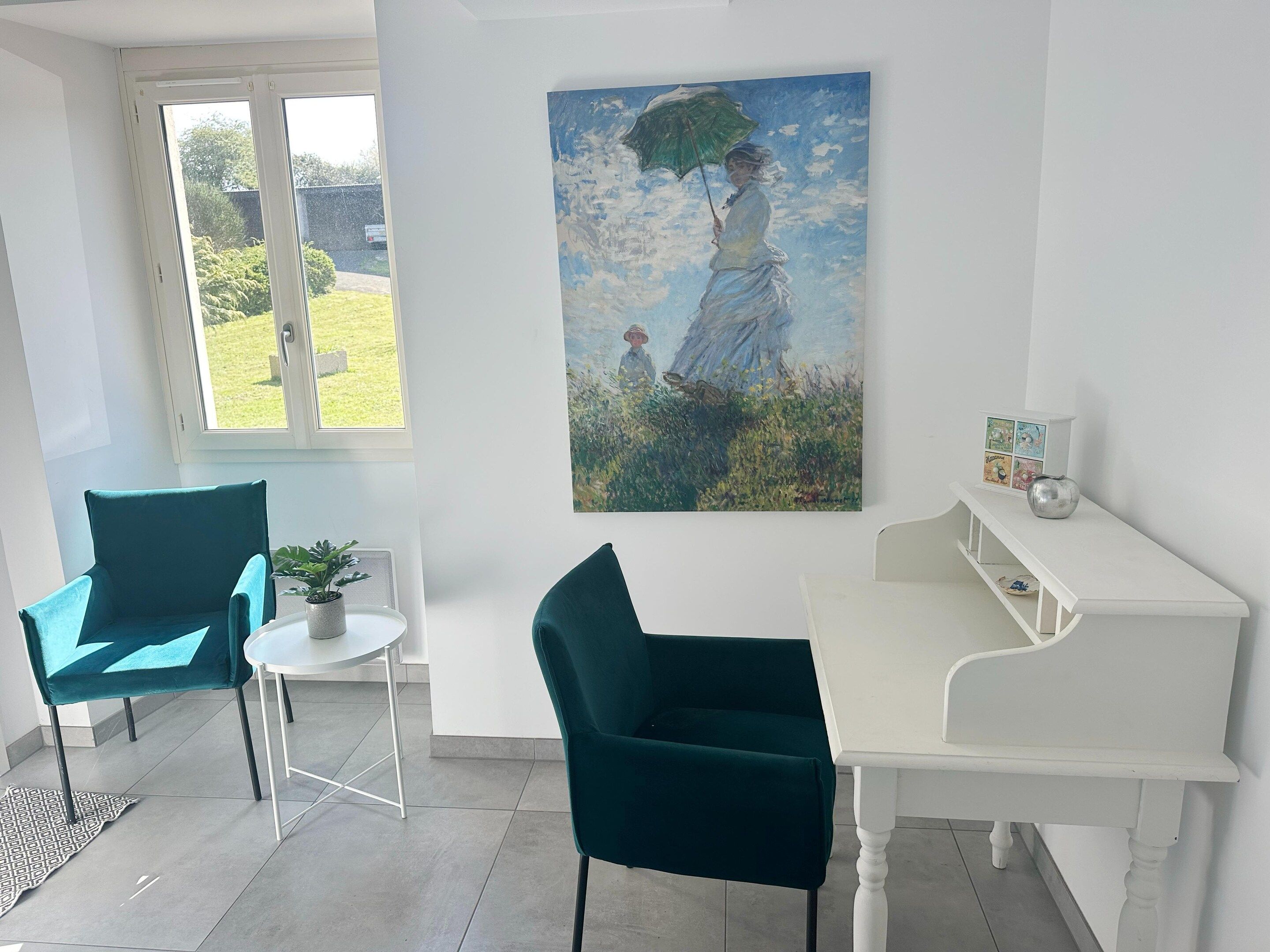 A room with a white desk, two teal chairs, a small table with a plant, and a painting of a woman with an umbrella.