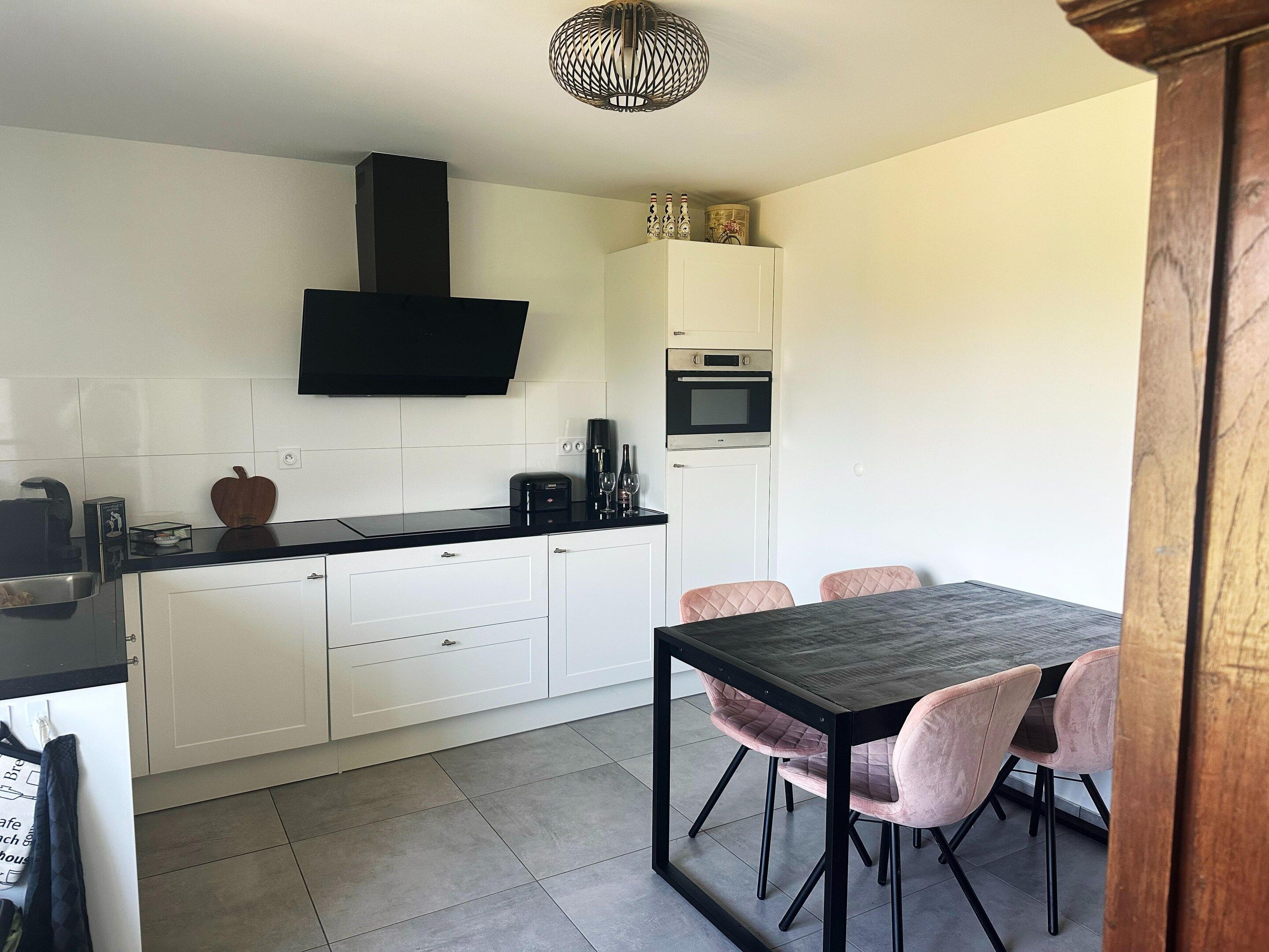 A modern kitchen with white cabinets, a black countertop, and a dining area with a table and chairs.