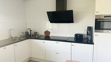 A compact kitchen with white cabinets, a black countertop, a coffee machine, and a microwave.