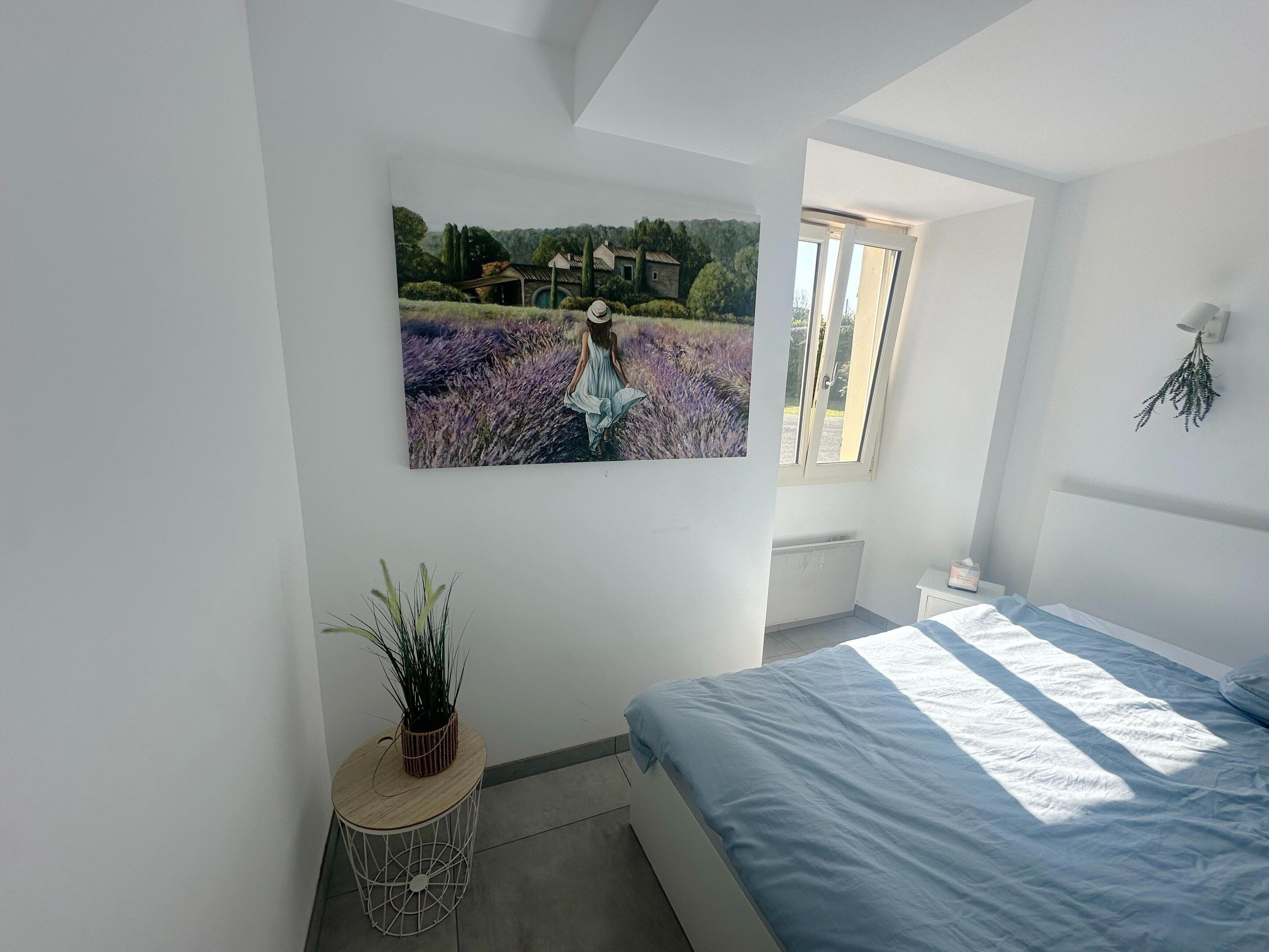 A bedroom with a bed, a window, a radiator, and a wall-mounted picture.