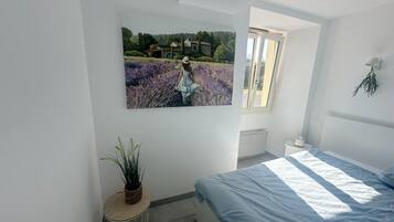 A bedroom with a bed, a window, a radiator, and a wall-mounted picture.