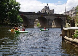 Une rivière où l’on peut faire du kayak, avec un pont de pierre en arrière-plan et une église au loin.