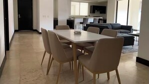 A modern living room with a dining area, a sofa, and a kitchen in the background. - Gorgeous 3-BR Condo in the heart of everything! (San Rafael de Escazú)
