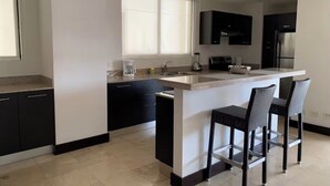 A modern kitchen with black cabinets, a white countertop, and a central island with bar stools. - Gorgeous 3-BR Condo in the heart of everything! (San Rafael de Escazú)