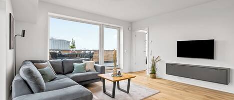 A modern living room with a grey sectional sofa, a wooden coffee table, and a flat-screen TV mounted on the wall.