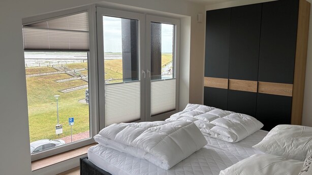 A bedroom with a large bed, a view of a grassy area, and a black headboard. - The View G03 Wyk - Sea view, terrace, garden furniture, 2nd floor, car parking (Dagebüll)