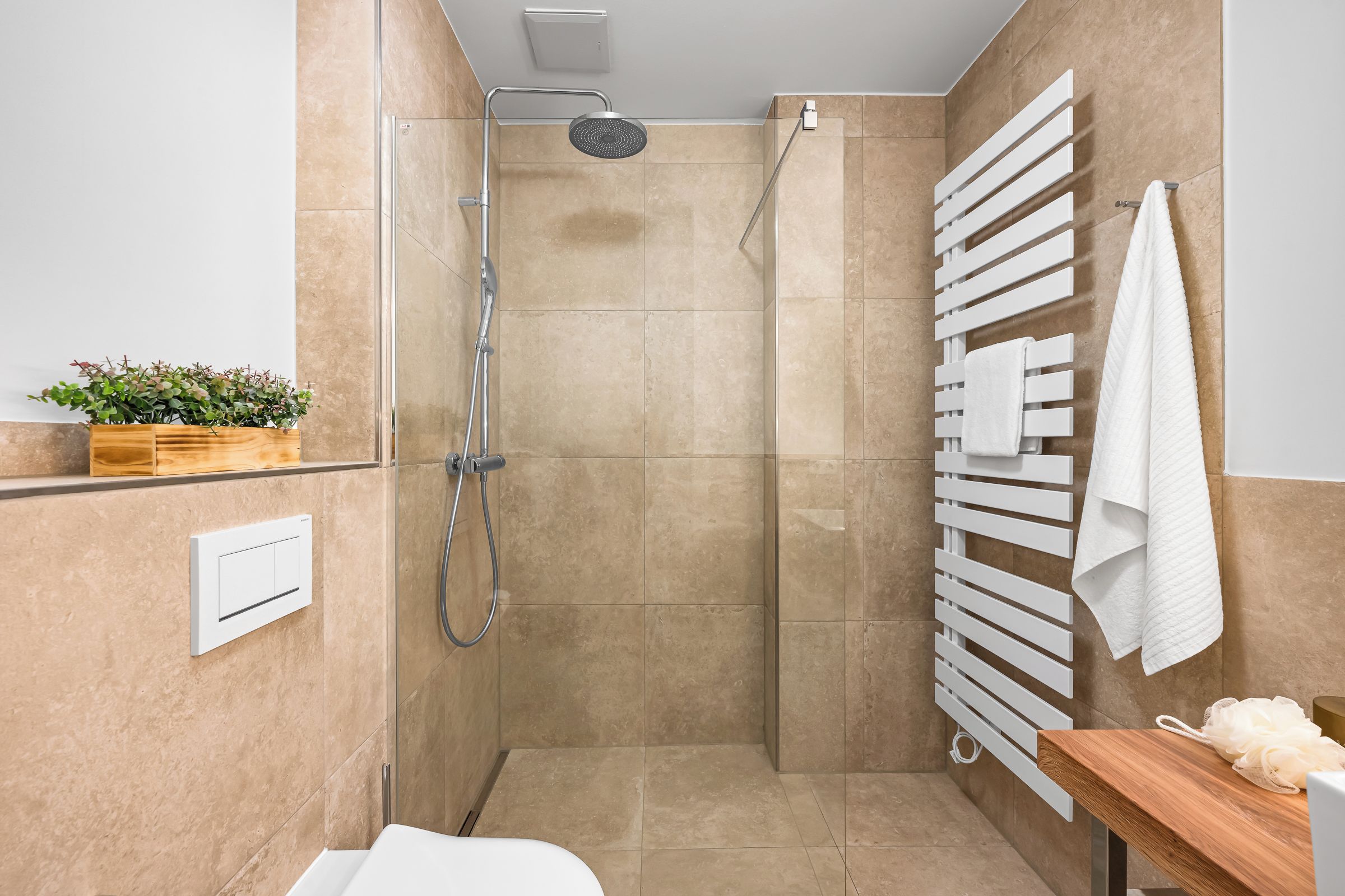 A modern bathroom with a shower, a towel rack, and a wooden shelf with a plant.