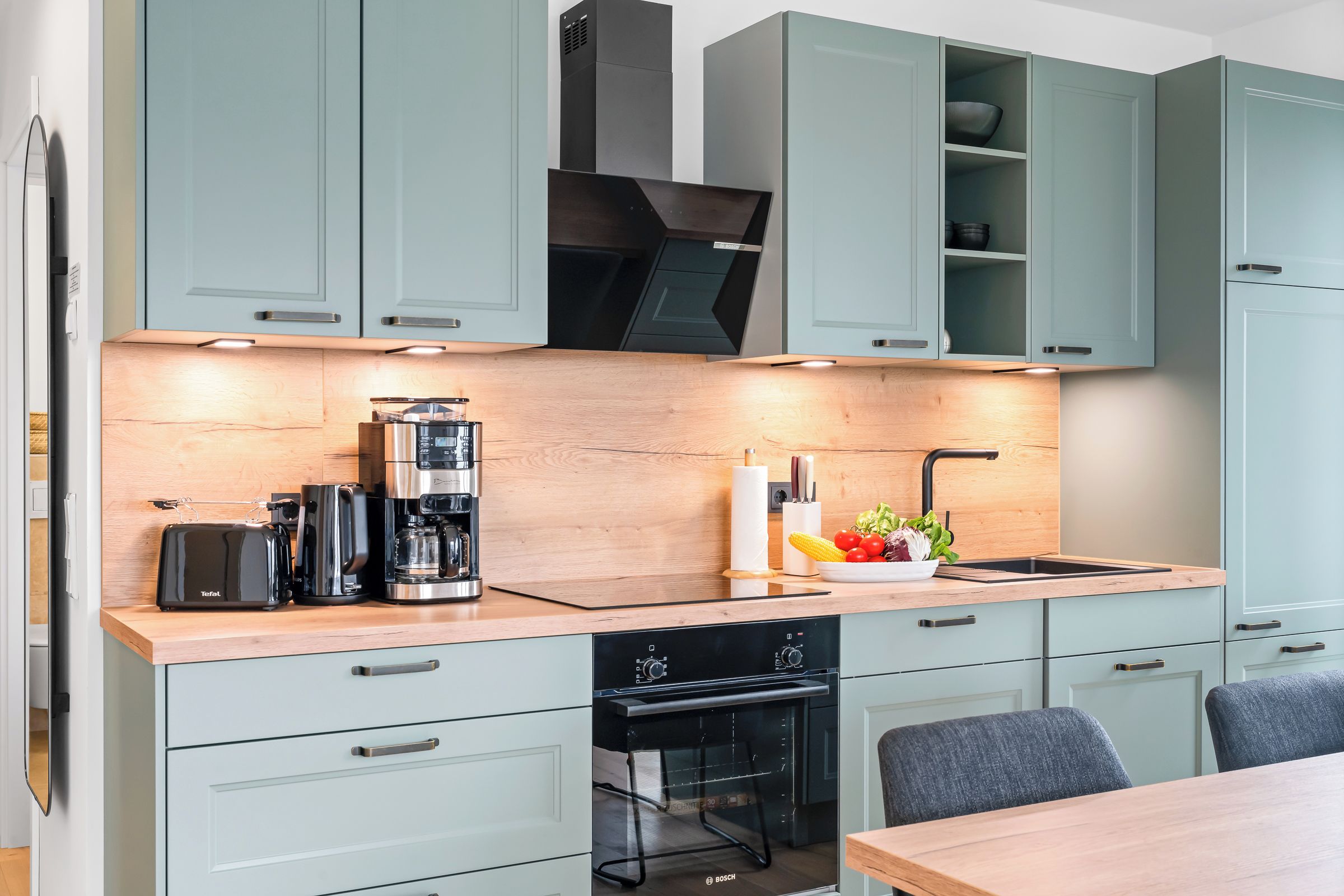 A modern kitchen with light blue cabinets, a wooden countertop, and a Bosch dishwasher.