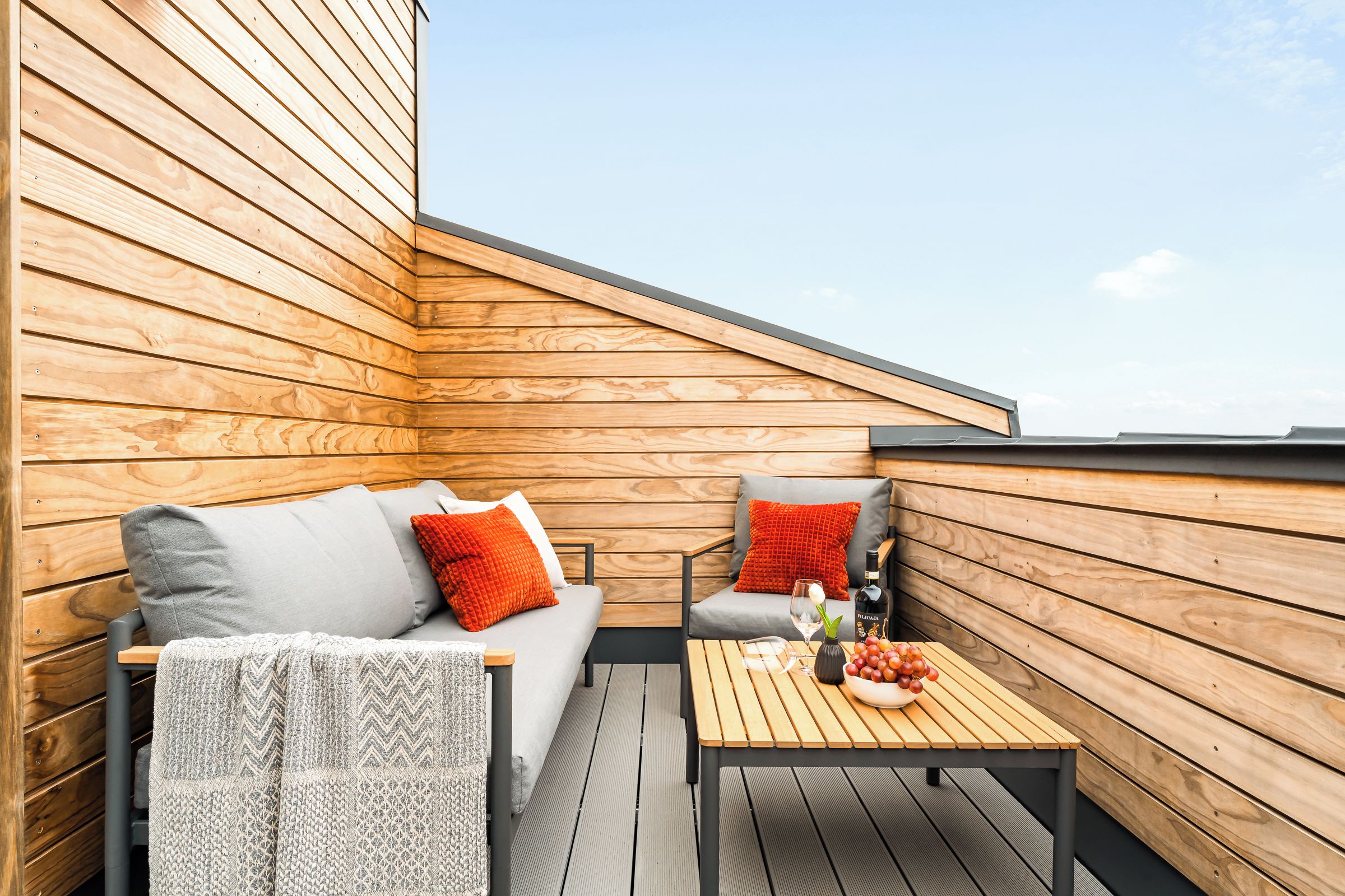 A wooden deck with a sofa and a table, both furnished with cushions.