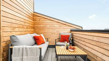 A wooden deck with a sofa and a table, both furnished with cushions.