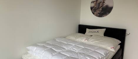 A bed with a white mattress and pillows, a black headboard, and a wall-mounted picture of plants.