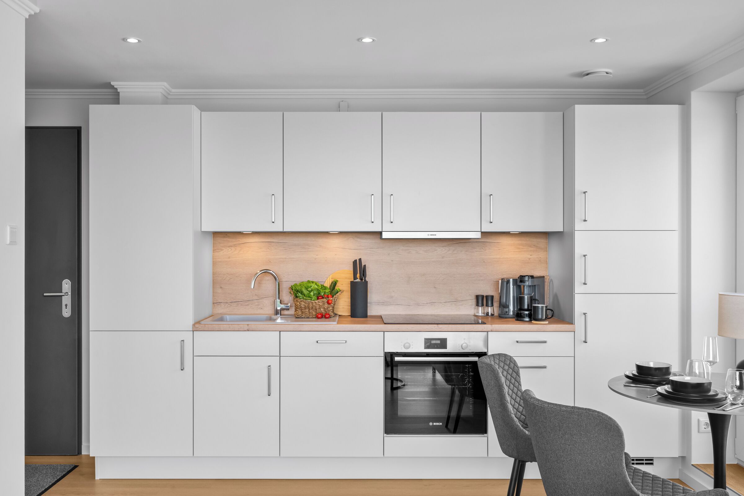 Eine moderne Küche mit weißen Schränken, einem eingebauten Backofen und einem Essbereich mit Tisch und Stühlen.