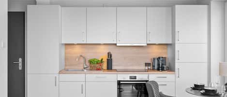 A modern kitchen with white cabinets, a built-in oven, and a dining area with a table and chairs.