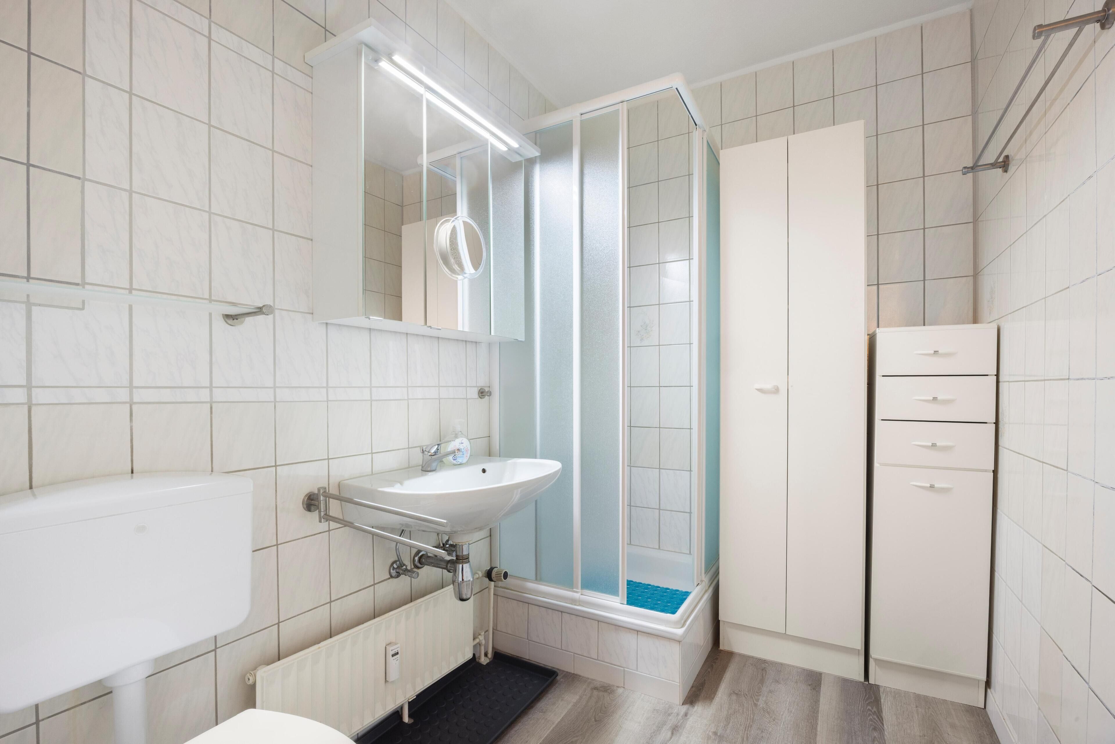 A modern bathroom with a white sink, mirror, and shower enclosure.
