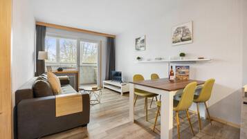 Ein modernes Wohnzimmer mit grauem Sofa, Couchtisch aus Holz und gelben Sesseln. Es gibt einen Esstisch mit Stühlen, einen Fernseher und einen Kamin.