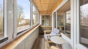 A room with large windows, a wooden ceiling, and a small table with a chair.