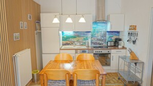A compact kitchen with a wooden dining table, two chairs, a stove, a sink, and a mural on the wall. - Comfortable vacation apartment with terrace and family facilities in Garding (Garding)