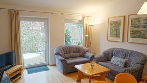 A living room with two patterned sofas, a wooden coffee table, a TV, and a large window with curtains. - Comfortable vacation apartment with terrace and family facilities in Garding (Garding)