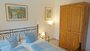 A bedroom with a bed, two pillows, a nightstand with a lamp, and a wooden wardrobe. - Künstlergarten Apartment 2: Comfortable vacation accommodation with terrace and garden i (Garding)