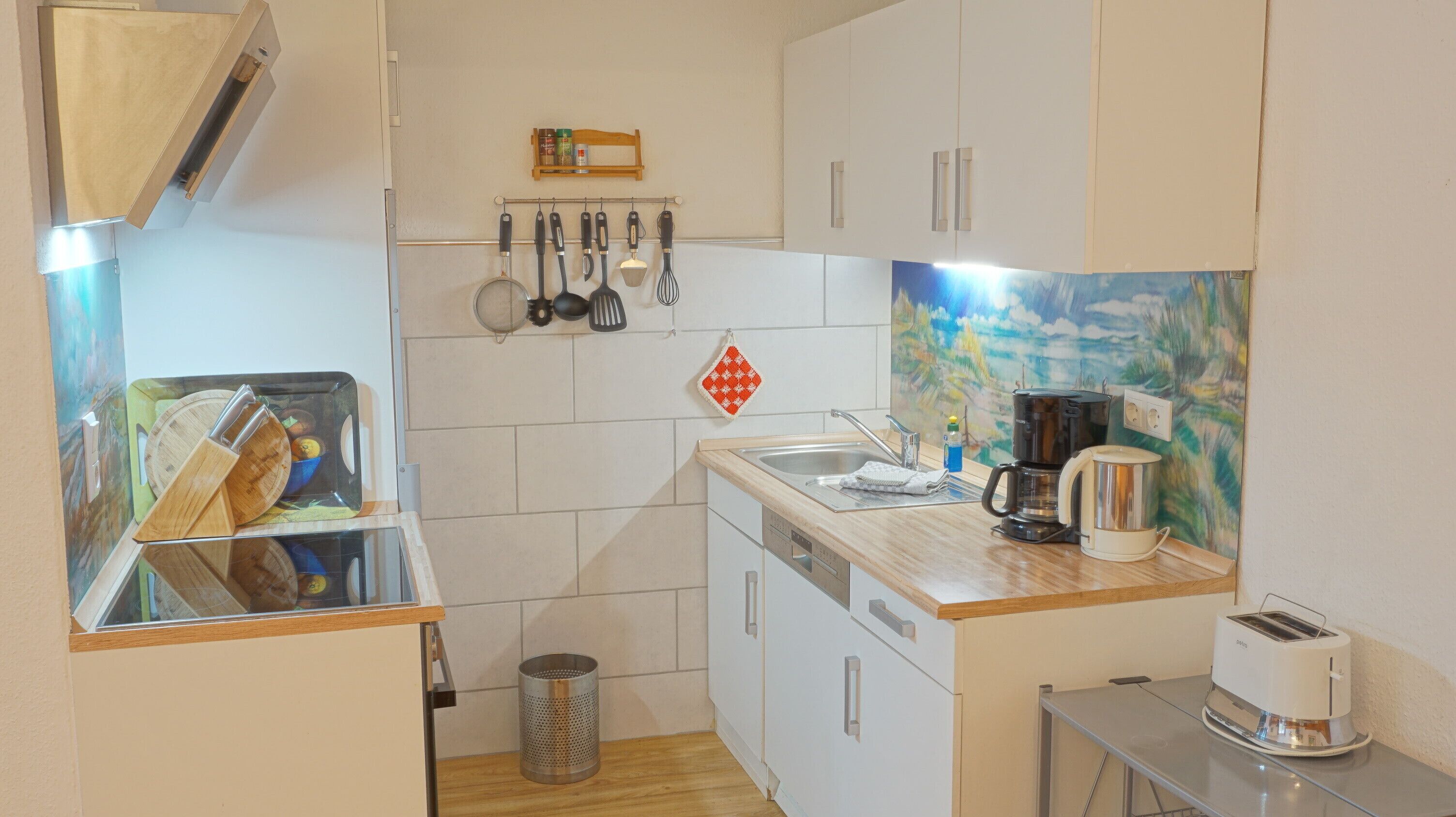 Eine kompakte Küche mit weißen Schränken, einer Holzausziehtafel, einer Kaffeemaschine, einem Toaster und einem Spülbecken.